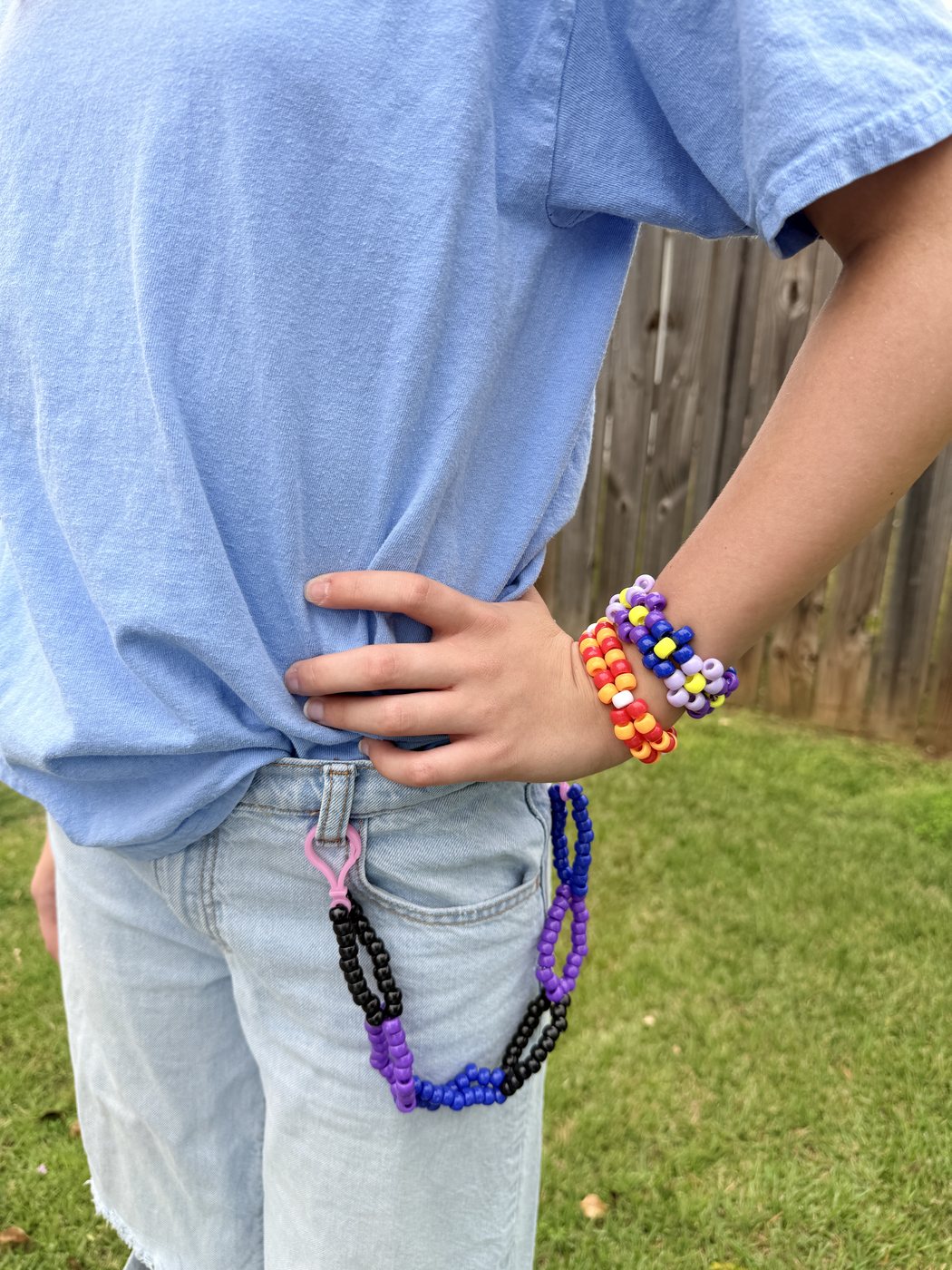 Beaded belt loop chain in purple, blue, and black clipped to jeans, with bracelets on the wrist