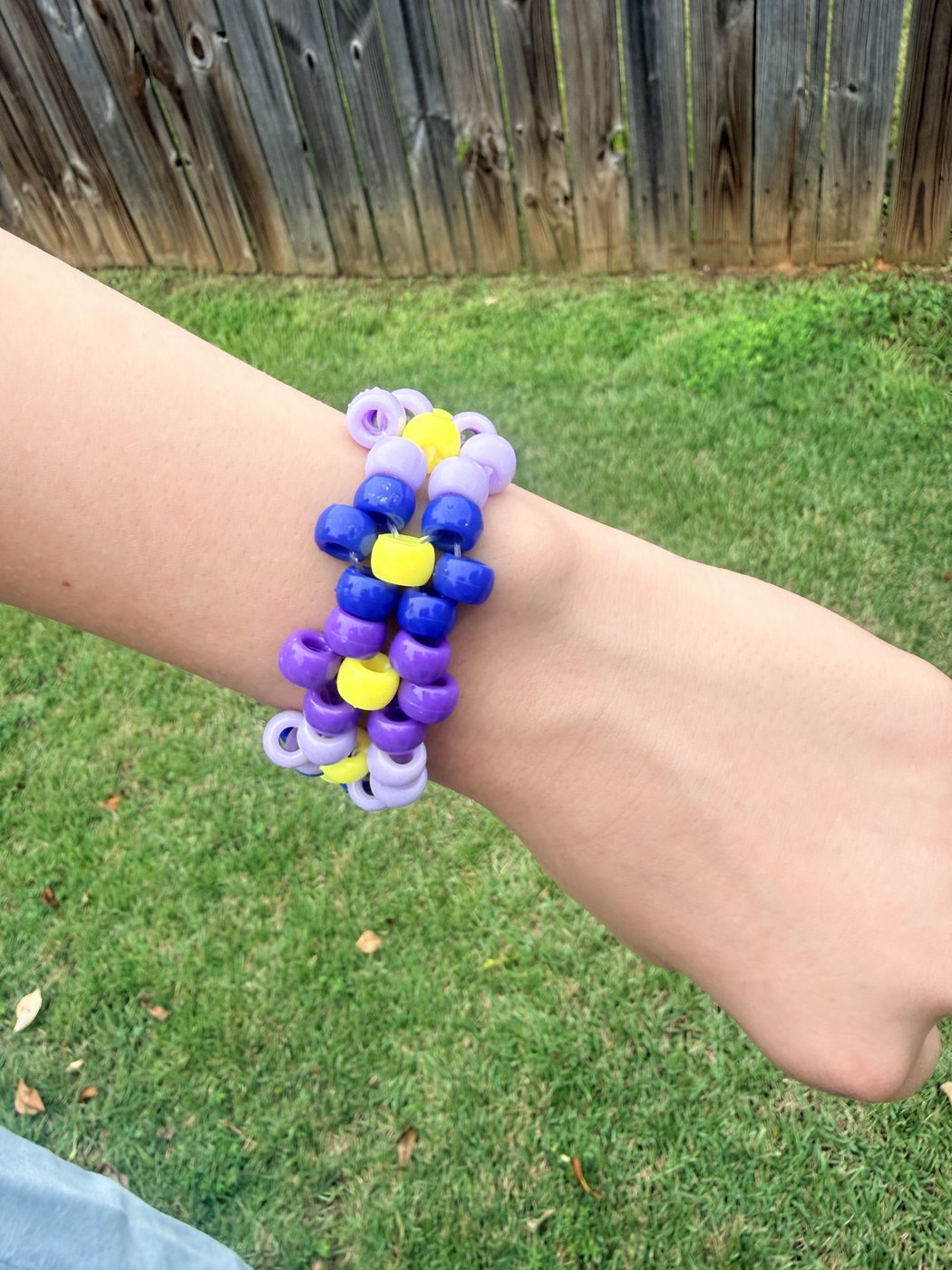 Flower-pattern pony bead bracelet in purples, blue, and yellow, worn on a wrist outdoors